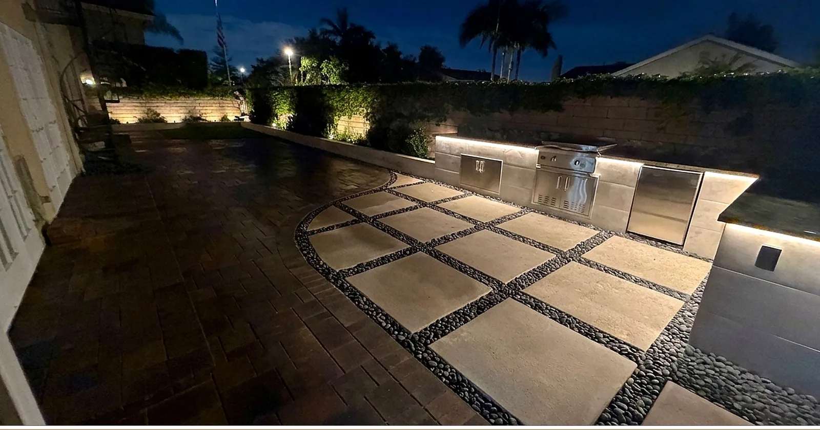 The finished patio at night with under-counter lighting glowing on the outdoor kitchen and pebble grid