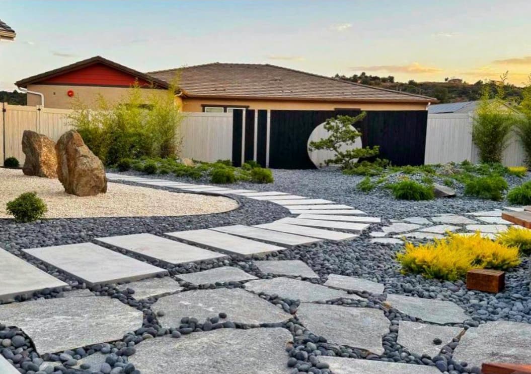 A contemporary Japanese garden with curved stepping stones, dark pebbles, boulders, planting and a timber screen with a circular feature.